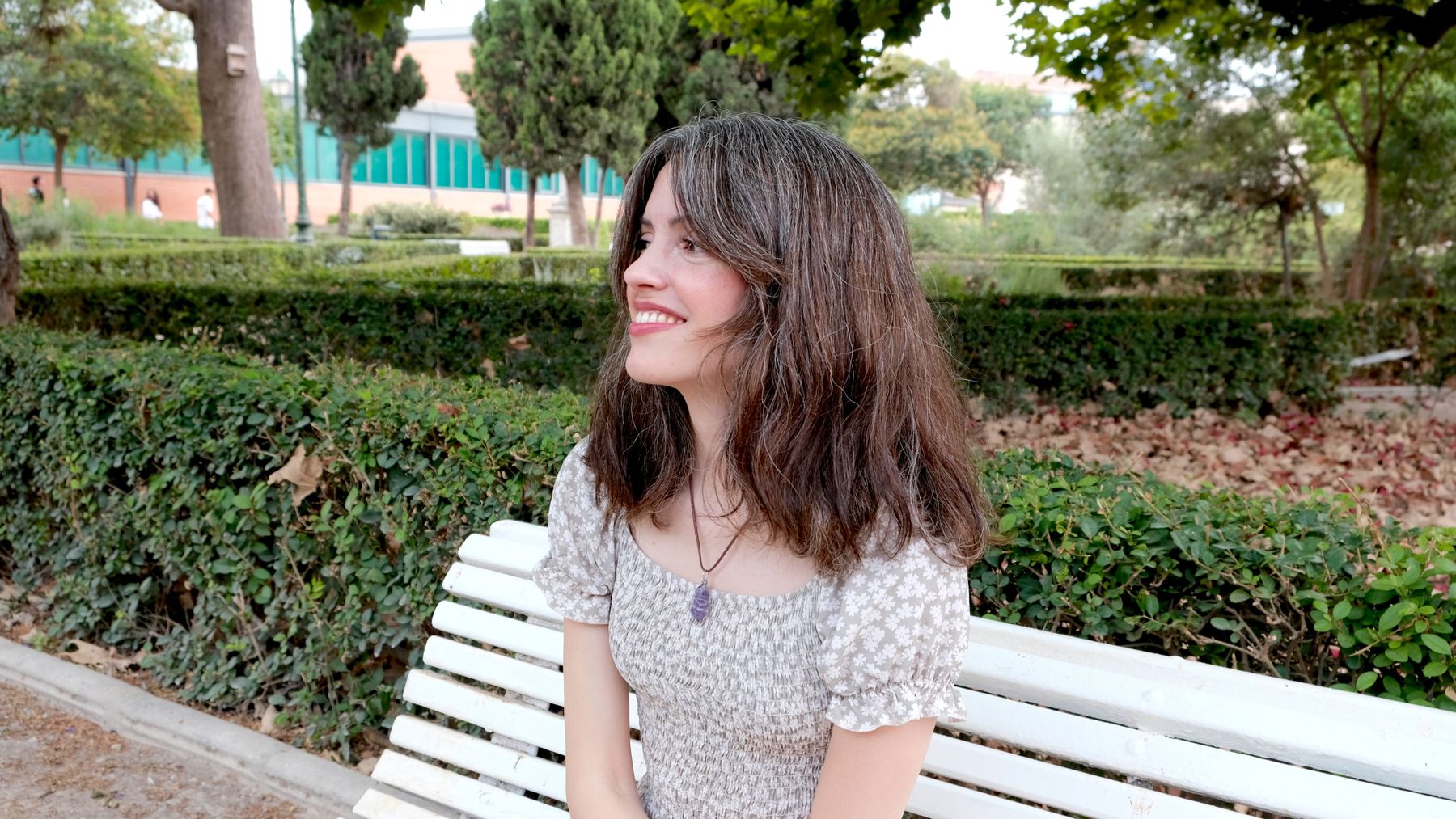 Andrea Picó sonriendo, sentada en un banco blanco de un parque